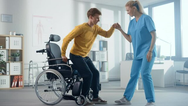 Hospital Physical Therapy: Determined Young Man with Injury Successfully Stands up from Wheelchair and Walks with Help of Rehabilitation Physiotherapist. Willpower, Grit, Strong Mindedness.Slow Motion