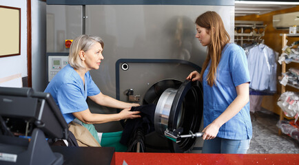Two adult female laundry employees working and taking out clothes from washing machine