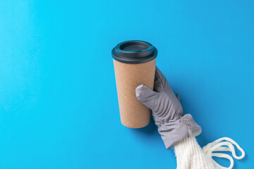 A woman's hand in a glove with a paper coffee glass on a blue background.
