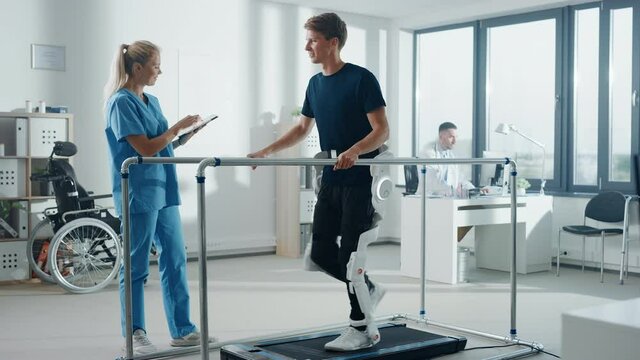 Modern Hospital Physical Therapy: Doctor Uses Tablet Computer, Helps Disabled Patient with Injury Walk on Treadmill Wearing Advanced Robotic Exoskeleton Legs. Physiotherapy Rehabilitation Technology