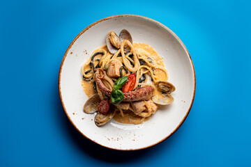 Seafood pasta with octopus and squid on a bright blue flat background, top view