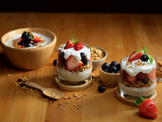 Glass and bowl of granola with Greek yogurt and fresh berries on wooden table