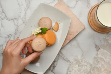 Female hand picking macaron to eat with milk on marble table