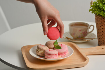 Female hand picking  French macarons from a plate on coffee table with tea cup