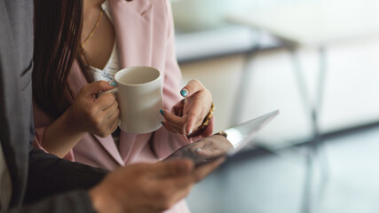 Two businesspeople hands holding tablet and coffee cup while consulting on their work