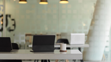 Workspace with laptops, office supplies and cup in glass partition office room
