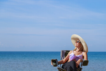 journey to the sea. girl in a bathing suit and hat sunbathing on the beach. tourist sitting on the sand. leisure wear. copy space