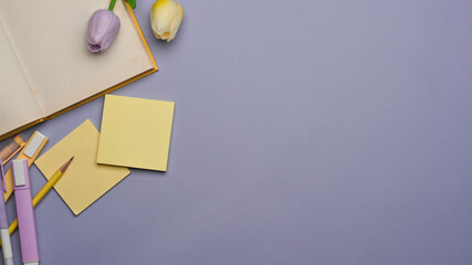 Workspace with stationery, book, flower and copy space on purple background