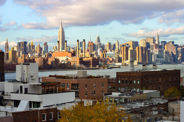Naklejka premium Blue sky, cloudy day shot of NYC, New York City in USA with sun shining over the skyscrapers, tall buildings in dense, built up environment. 