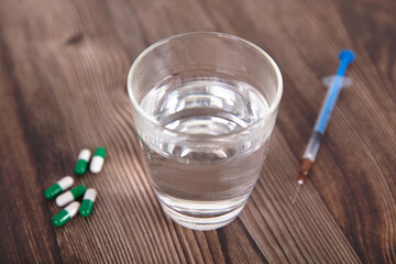 A glass of water and a few capsules and medical needles are on the table