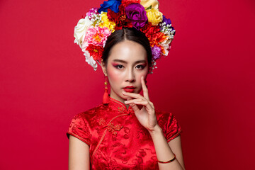 Gorgeous Asian woman in traditional Cheongsam dress with colorful make up and flower wreath on head in red isolated studio background