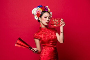 Beautiful Asian woman in oriental qipao dress with flower wreath on head holding red envelopes and...