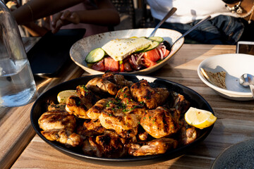 Authentic photo of Greek grilled chicken with out of focus greek salad in the background under golden light sunlight. People can be seen