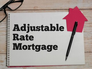 Property concept. Top view text Adjustable Rate Mortgage written on notebook with pen,house cupboard and eye glasses on wooden table.