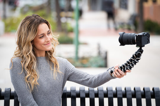 Young Millennial Women with Blonde Brunette Hair Looking at Mirrorless Camera on Tripod