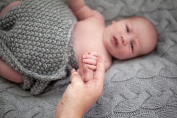 Cute baby lies on knitted grey blanket. New born baby smiling happily at camera. Care body concept