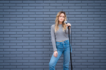 Young Blonde Female Comedian Against Blue Grey Brick Wall with Microphone and Expressions