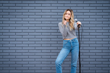 Young Blonde Female Comedian Against Blue Grey Brick Wall with Microphone and Expressions