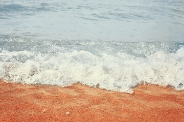 Sandy beach with waves from the sea. Blue water in the beautiful ocean. White foam waves on hot sand.