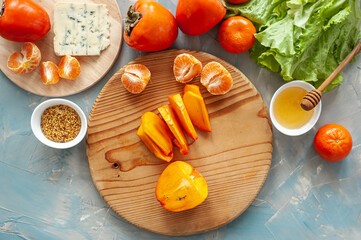 Ingredients and the process of making a vitamin winter salad with persimmons, tangerines and blue cheese. Step by step. View from above.