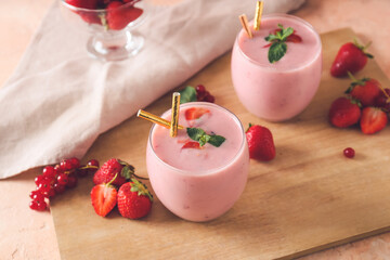 Glasses of tasty smoothie with strawberry and cranberry on wooden board