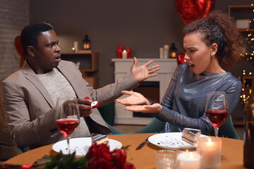 Confused African-American man proposing to his displeased beloved on Valentine's Day at home