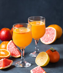 Citrus juice in two glasses and fresh fruit tangerine, orange, grapefruit and lemon on a dark gray background