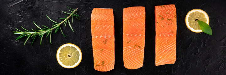 Salmon panorama with lemons and herbs, top shot on a black background