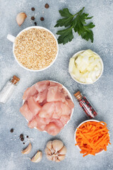 Raw ingredients for cooking pilaf, Brown rice and chicken fillet, grated carrots and chopped onions, pepper tomato garlic herbs and spices. Gray background, top view.
