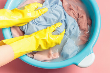 Female hands in rubber gloves washing pink clothes in basin, top view