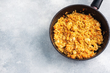 Delicious Asian pilaf, stewed rice with vegetables and chicken in a frying pan. gray concrete...