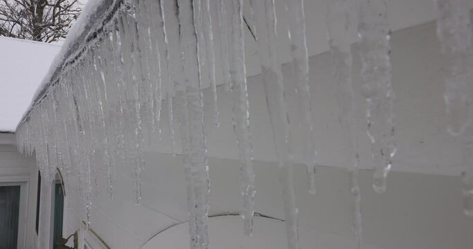 Tight handheld pull of dripping icicles hanging from soffit on house in the winter.
