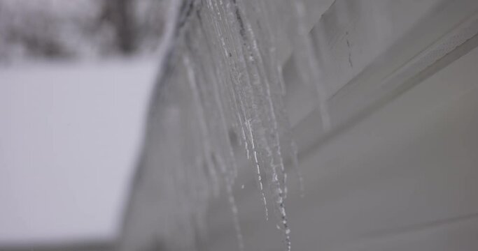Tight handheld push of dripping icicles hanging from soffit on house in the winter with narrow depth of field.