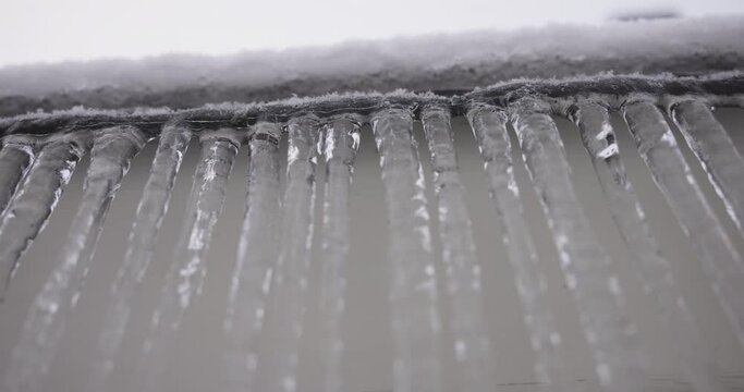 Pan of dripping icicles hanging from soffit on house, shot from below.