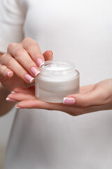 Close-up of a young girl holding an open jar of cosmetic cream in her hands. Skin care and beauty concept.