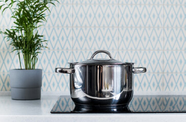 A metal pot on an electric induction cooker in a modern kitchen. Copy space.