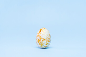 Happy Easter. One easter egg trendy colored gold on blue background. Copy space. Minimal style.