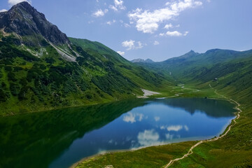 Naklejka na ściany i meble hiking trail on a deep blue mountain lake in a green landscape in the summer