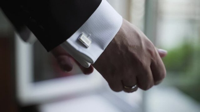 Male hands close up. A man in classic suit and white shirt straightens cufflinks on his sleeves