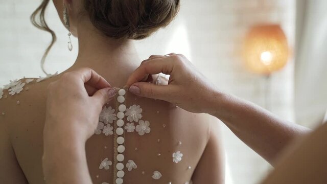 Mother dresses bride in dress and fastens button on the back. Gathering the bride in the morning