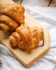 Two french croissants on the wooden cutting board decorated with wheat and napkin