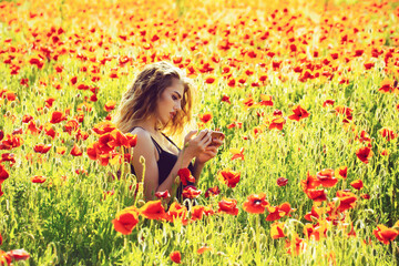 Naklejka na ściany i meble Beautiful teenager girl in blossom park. Woman in field of poppy making selfie photo.