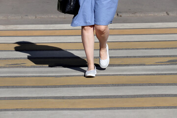 Female legs on pedestrian crossing, street safety concept. Woman in a summer dress walking on the crosswalk, shadow on zebra