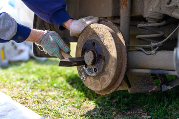men's gloved hands repair of car drum brake himself. disassembles a jammed disk with a hammer. repair of broken car drum brake disassembled outdoor