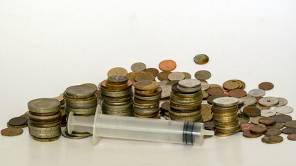with metal coins of various shapes, countries and values, an empty medical syringe in the foreground