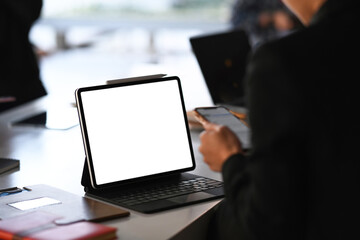 Close up view of tablet computer on office table with businesswoman texting on a smart phone.