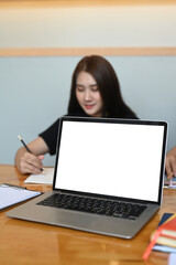 Laptop computer with blank screen and businesswoman working in background.