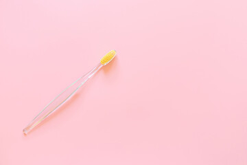 Toothbrush with yellow bristles on a pink background. Oral hygiene, dentistry, teeth cleaning concept. Minimalism, top view, copy space.