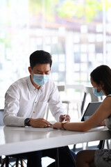 Two business people wearing protective mask discussing marketing strategy at office table.