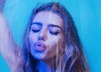 Sensual Kiss. Spa and beauty. spa treatment of young woman with long curly hair holding window glass with water drops.